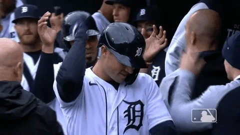 GIF of Tigers player Spencer Torkelson walking past teammates in the dugout while making a hand gesture