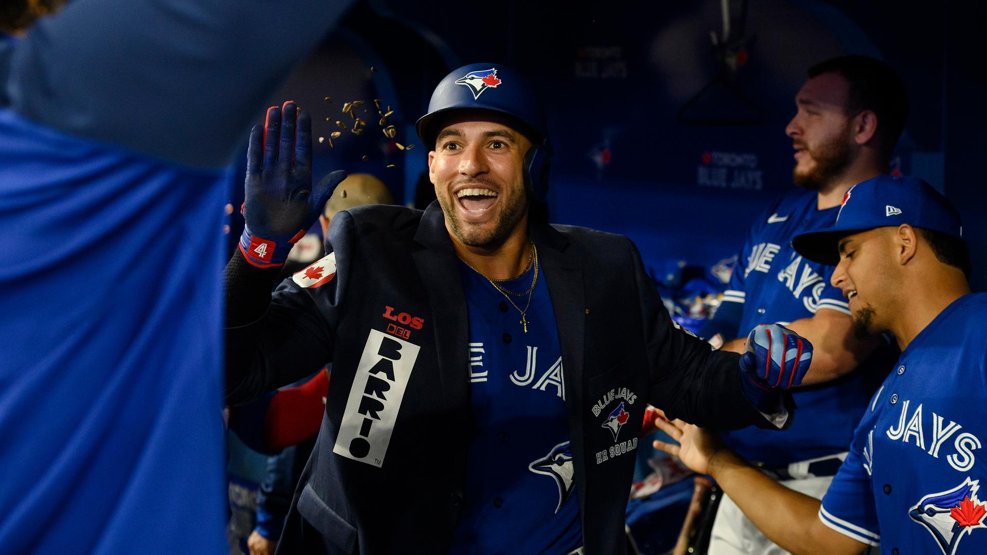 A smiling George Springer wears a jacket with patches over his uniform as he receives high-fives in the dugout