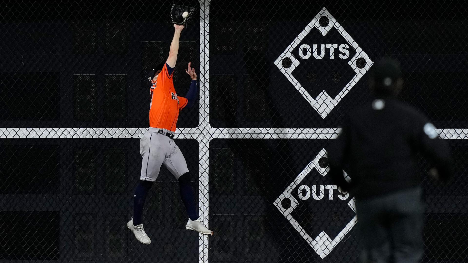 Chas McCormick leaps up against the outfield fence to catch a fly ball