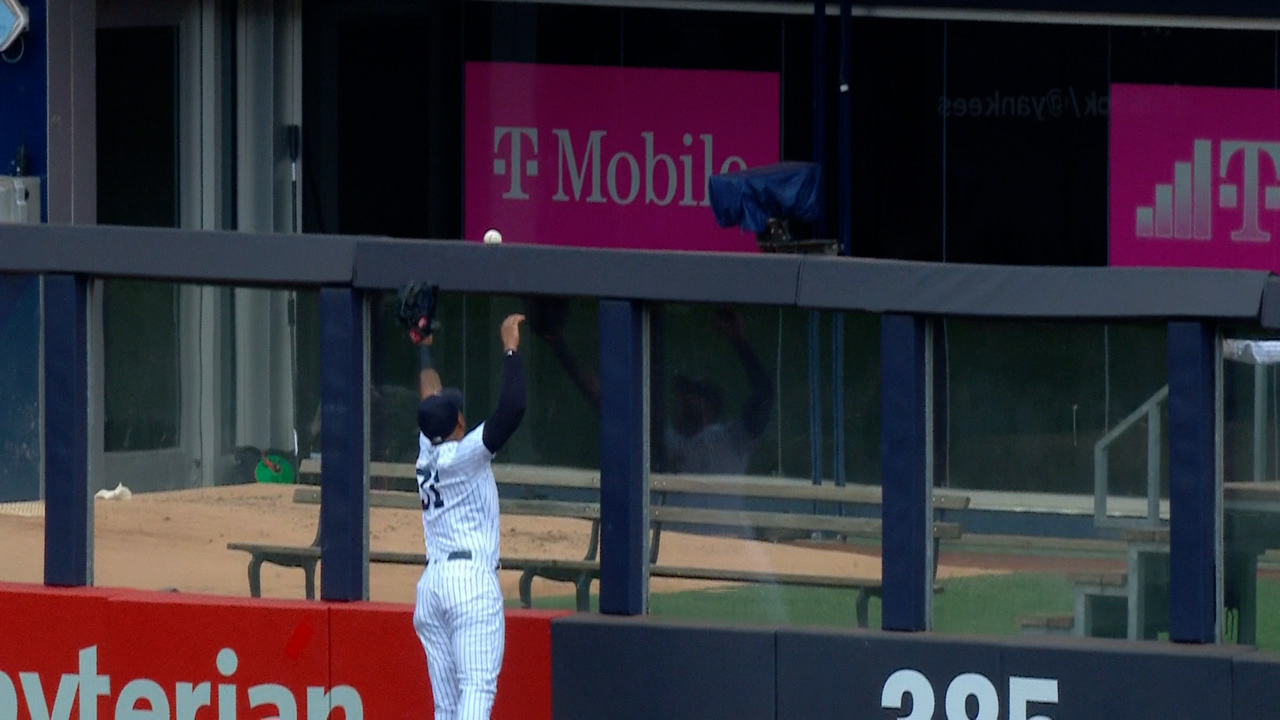 A Yankee outfielder reaches up in vain as a ball is shown atop the edge of the outfield wall just before going over for a home run