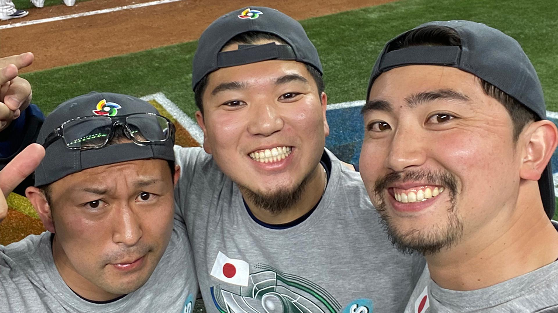 Three men look up at the camera smiling with caps on backward