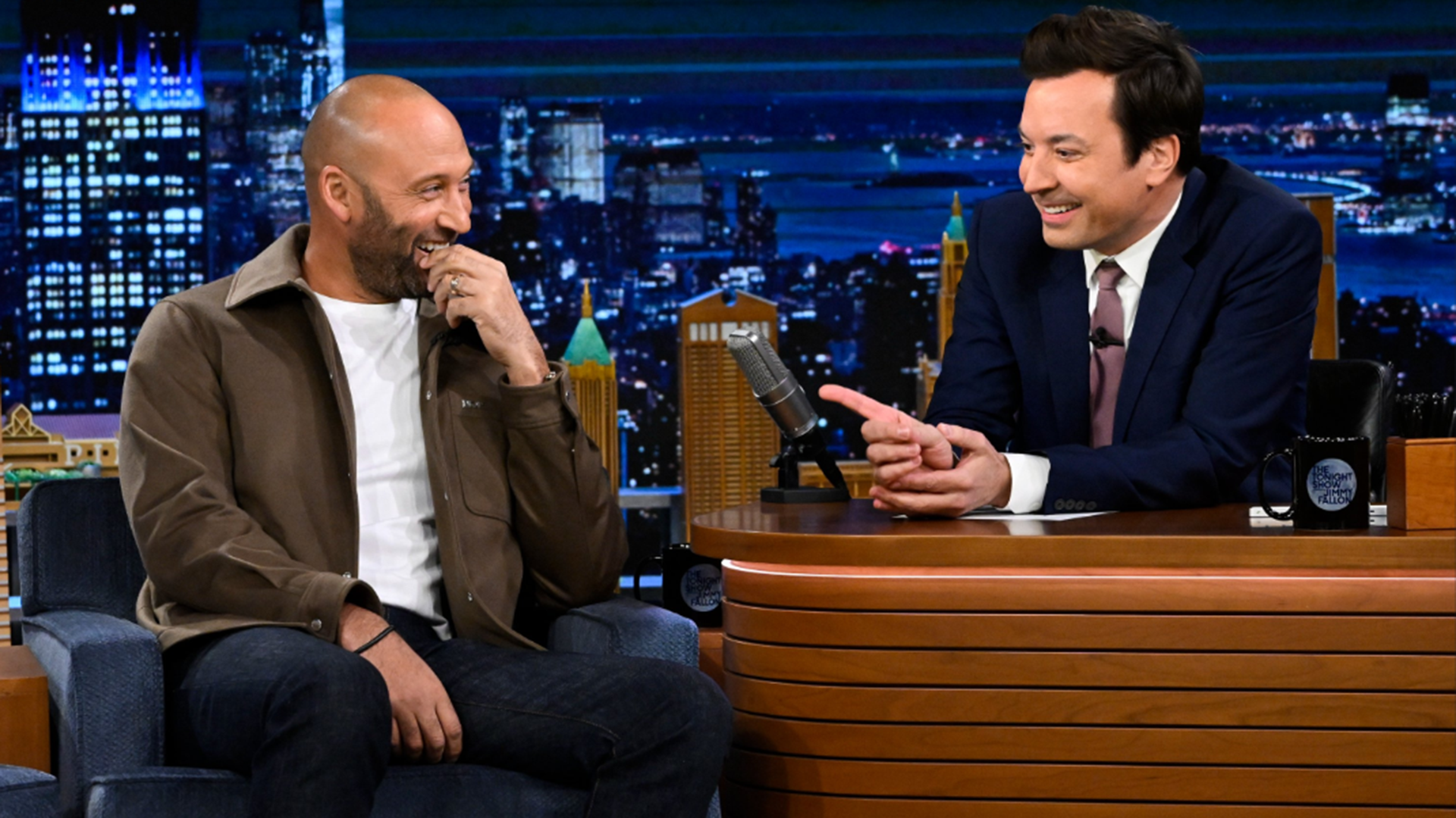 Derek Jeter in a chair on set with Jimmy Fallon, sitting behind a desk