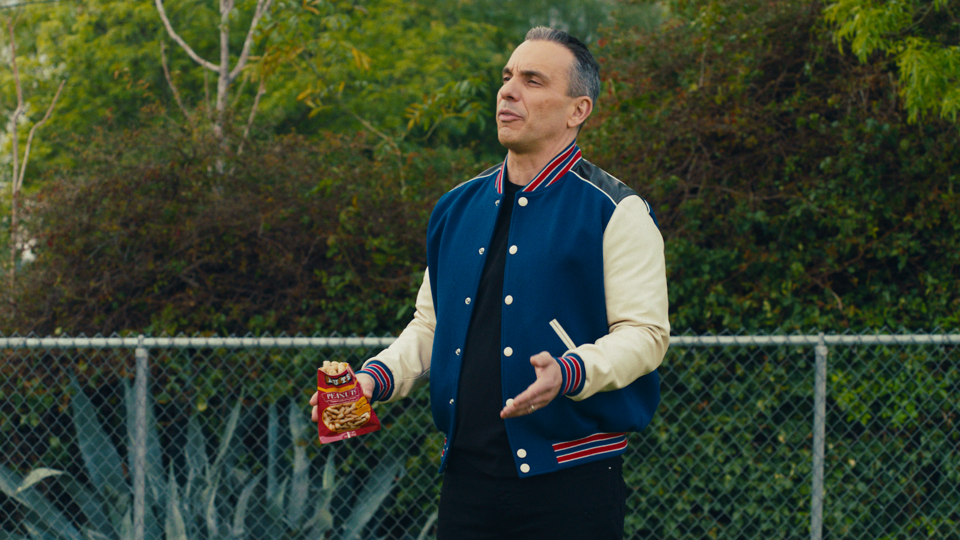 A screenshot of a man on a field holding a back of peanuts