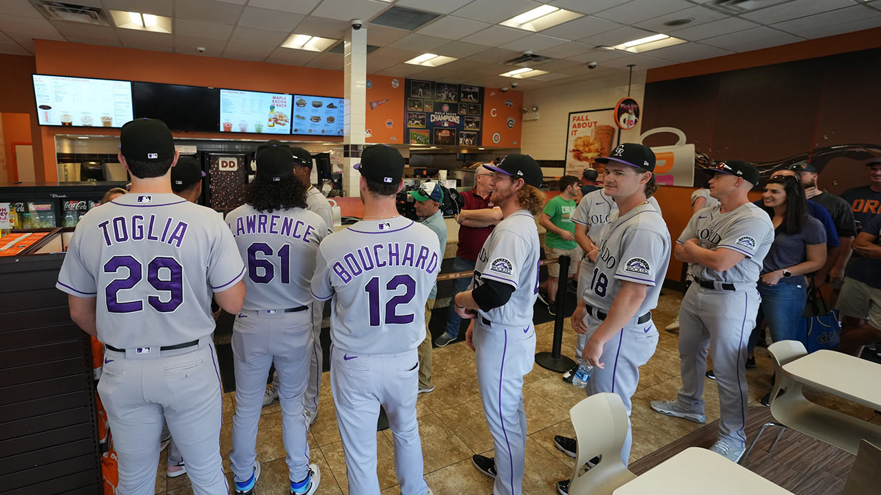 Rockies players in full uniform wait in line for coffee at a restaurant