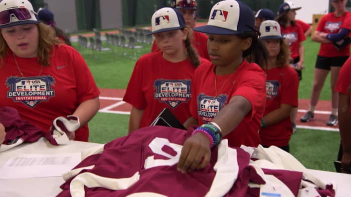 Girls pick up jerseys at a baseball camp