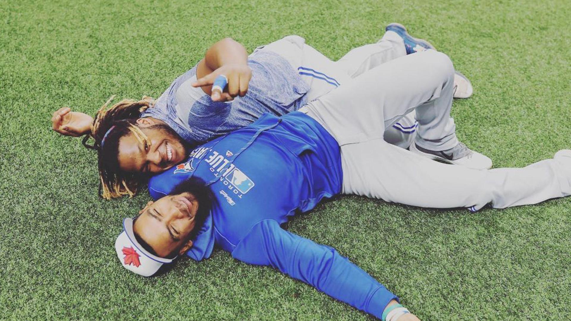 Vladimir Guerrero Jr. and Teoscar Hernández lying down on the outfield grass